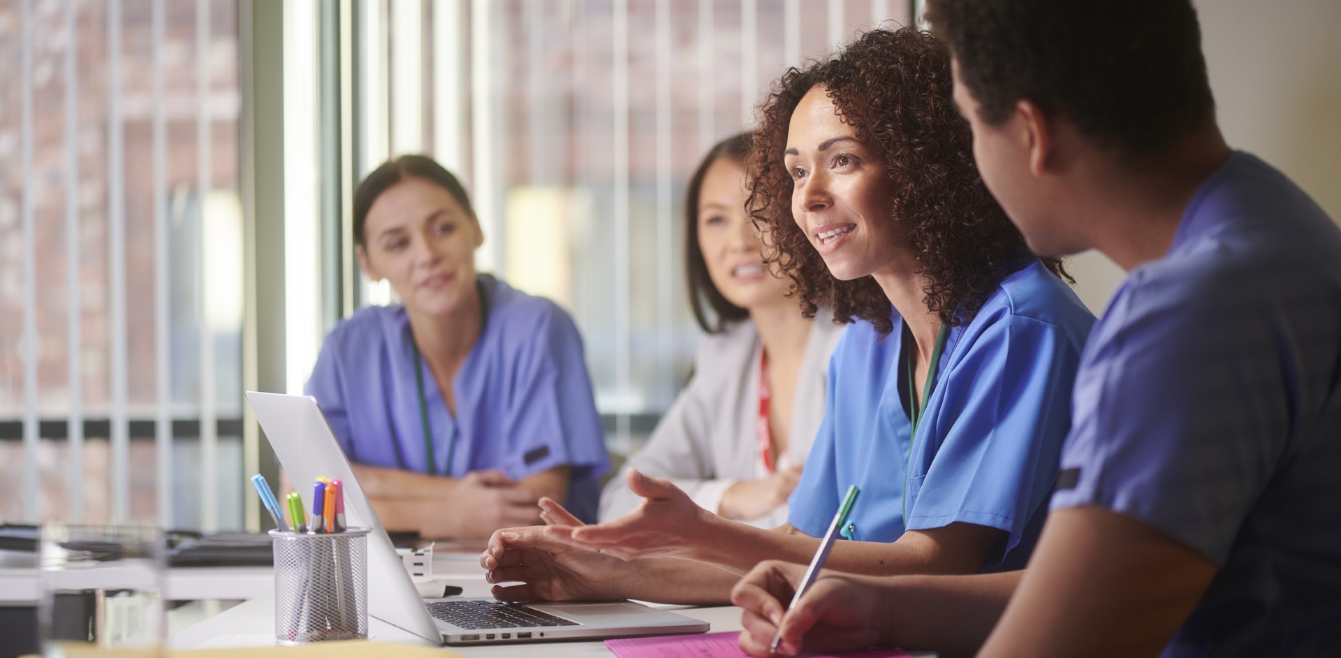 Teammeeting im Gesundheitsbereich: Personen tauschen sich aus, eine Person schreibt Notizen.